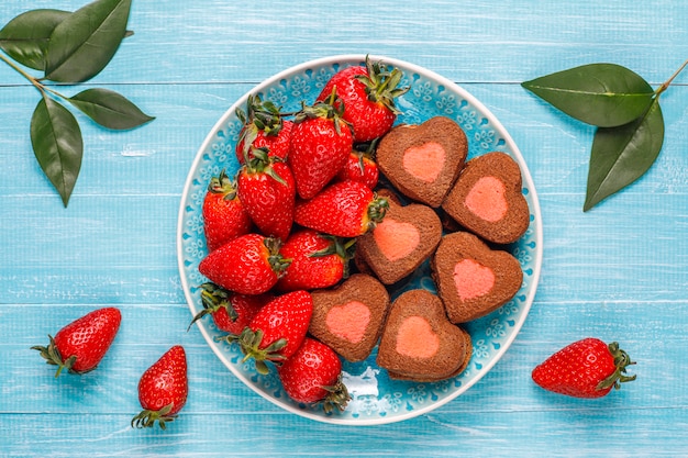 Galletas de chocolate y fresa en forma de corazón con fresas frescas, vista superior