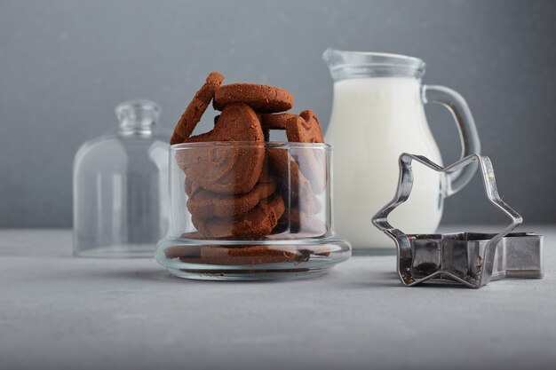 Galletas de chocolate y un tarro de leche sobre fondo azul.