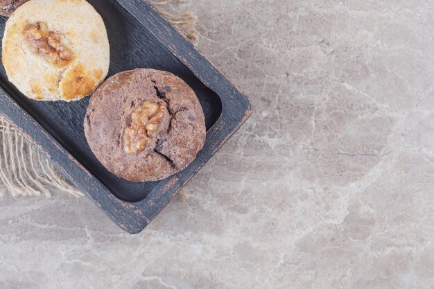 Galletas con coberturas de nueces en una pequeña bandeja negra sobre mármol