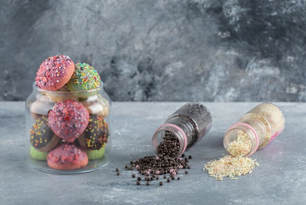 Galletas de colores con caramelos en frasco de vidrio con montón de chispitas.