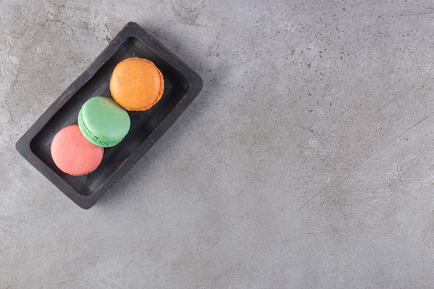 Galletas de colores en una placa de madera, sobre la mesa de mármol.