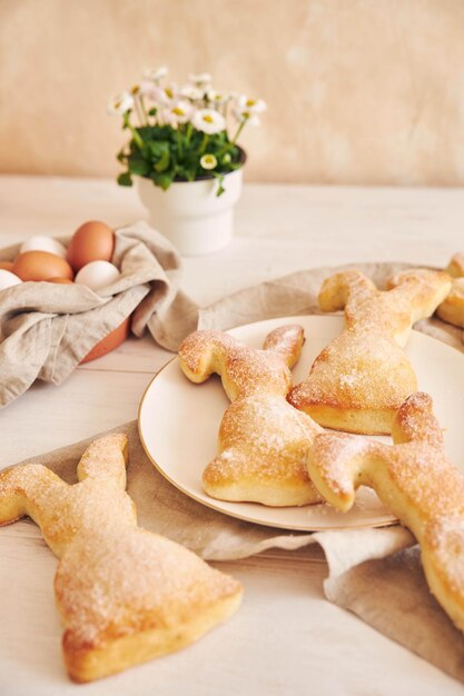 Galletas de conejito de Pascua, huevos de Pascua y flores en maceta sobre una mesa de madera blanca