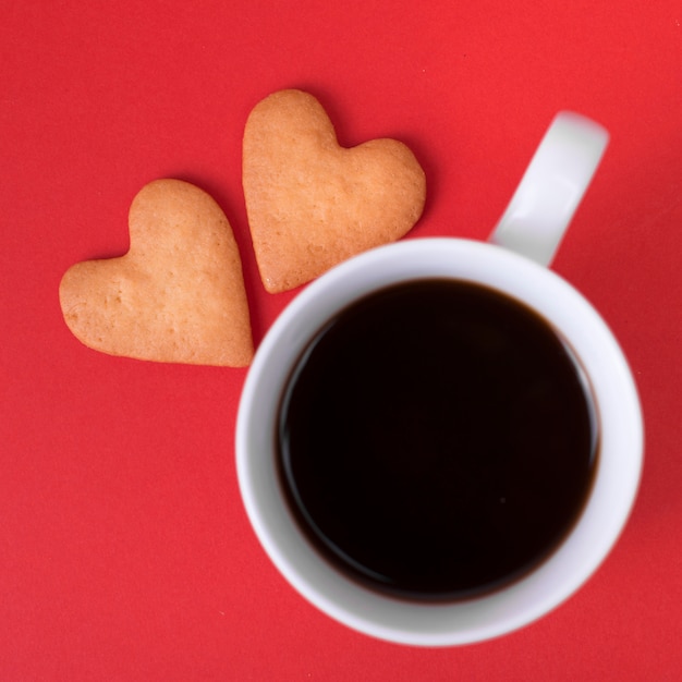 Galletas de corazón con taza de café en la mesa roja