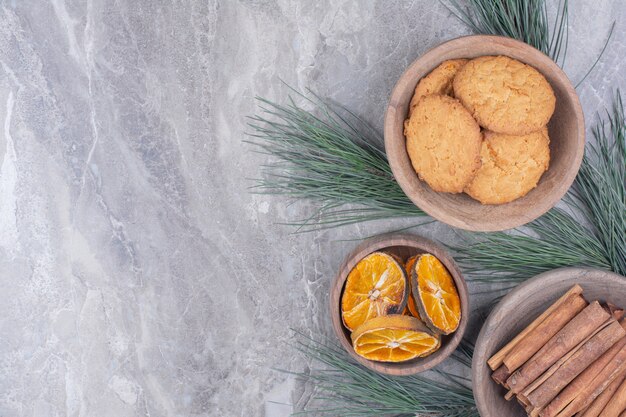 Galletas crujientes en una taza de madera con ramas de canela y rodajas de naranja secas alrededor.