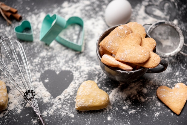 Galletas del día de San Valentín con harina y utensilios de cocina.