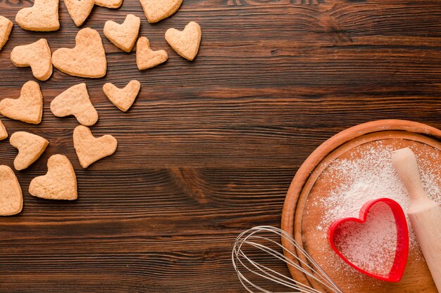 Galletas del día de San Valentín con utensilios de cocina sobre fondo de madera