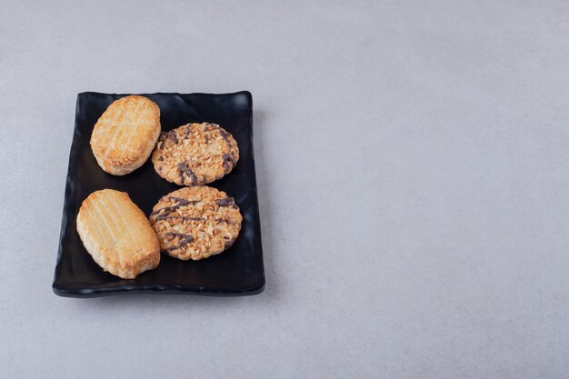 Galletas dulces caseras en placa de madera sobre mesa de mármol.