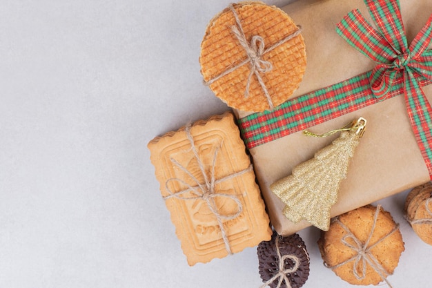 Foto gratuita galletas dulces en cuerda con regalo y juguete dorado de navidad en mesa blanca