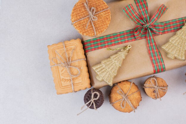 Galletas dulces en cuerda con regalo y juguete dorado de Navidad sobre superficie blanca