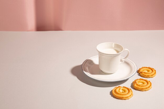 Galletas dulces dispuestas alrededor de la taza de leche sobre el escritorio blanco