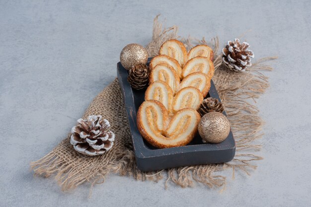 Galletas escamosas y adornos navideños en una pequeña bandeja sobre la superficie de mármol