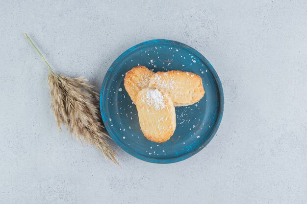 Galletas escamosas en un plato azul junto a un tallo de pasto de plumas sobre fondo de mármol.