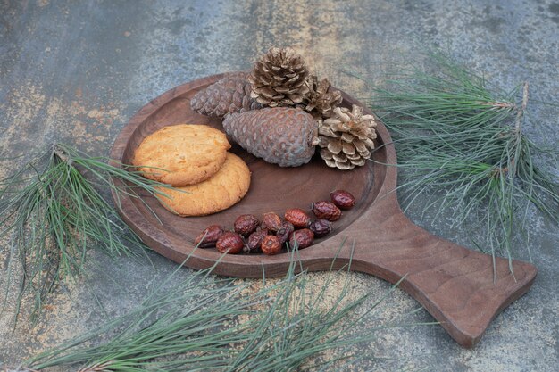 Galletas, escaramujos secos y piñas sobre tabla de madera. Foto de alta calidad