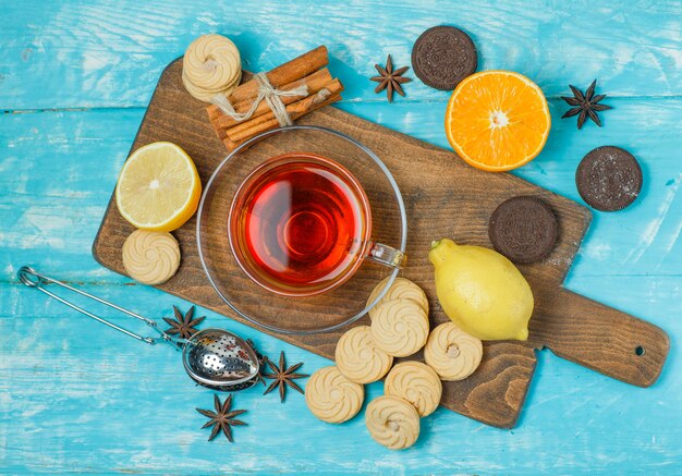 Galletas con especias, té, limón, naranja, colador en azul y tabla de cortar