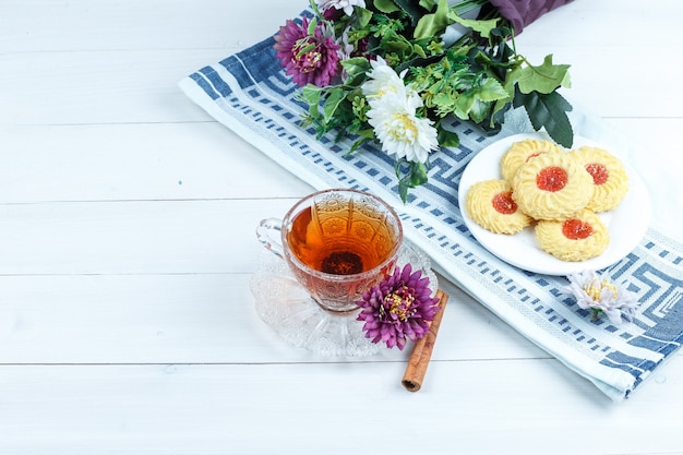 Galletas, flores en un mantel con canela, taza de té