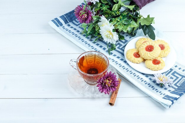 Galletas, flores en un mantel con canela, taza de té