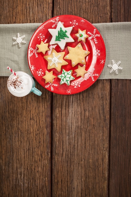 Galletas con forma de estrella sobre un plato rojo y una taza con nata