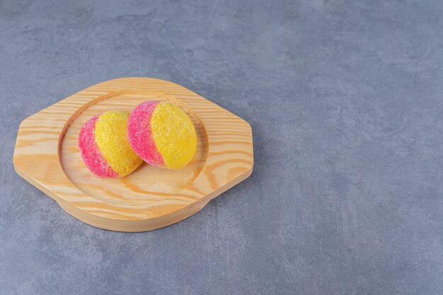 Galletas en forma de melocotones en una placa de madera sobre una mesa de mármol.