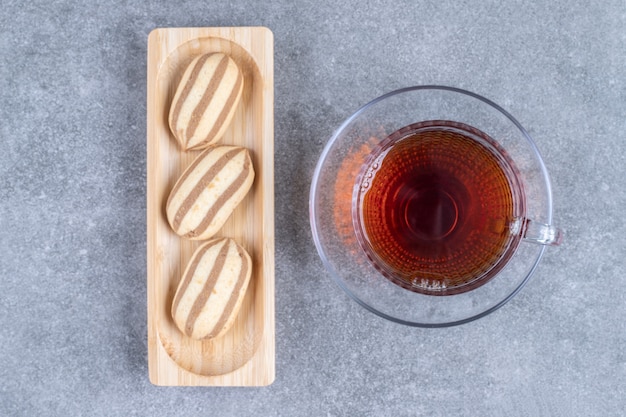 Galletas de forma ovalada en placa de madera con taza de té