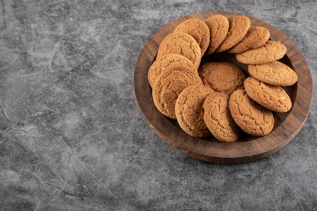 Galletas frescas caseras en bandeja de madera sobre mesa gris.