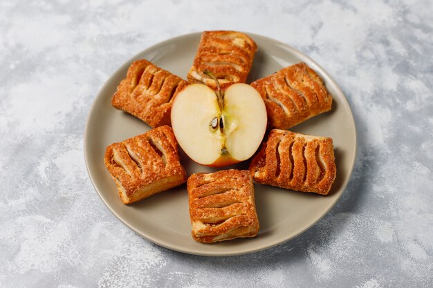 Galletas de hojaldre rellenas de mermelada de manzana y manzanas rojas frescas sobre hormigón ligero