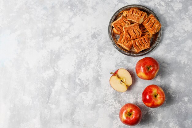 Galletas de hojaldre rellenas de mermelada de manzana y manzanas rojas frescas sobre hormigón ligero