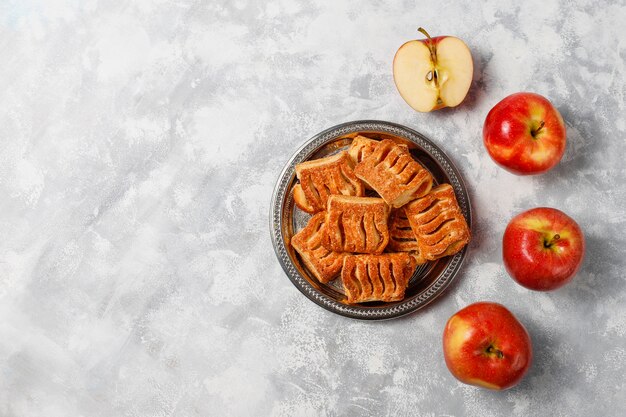 Galletas de hojaldre rellenas de mermelada de manzana y manzanas rojas frescas sobre hormigón ligero