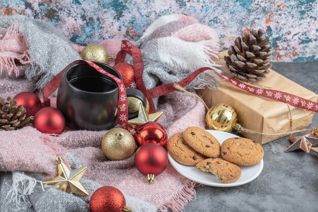 Galletas de jengibre crujientes en un platillo blanco con una taza de bebida y adornos navideños alrededor