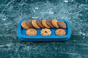 Foto gratuita galletas lisas y de chocolate en una bandeja de madera, sobre el fondo azul. foto de alta calidad