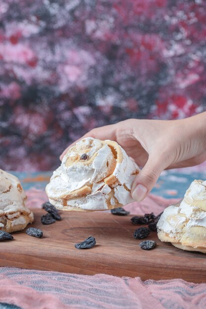 Galletas de merengue blanco con pasas negras sobre una tabla de madera.