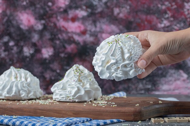 Galletas de merengue floral blanco con coco en polvo sobre una tabla de madera.