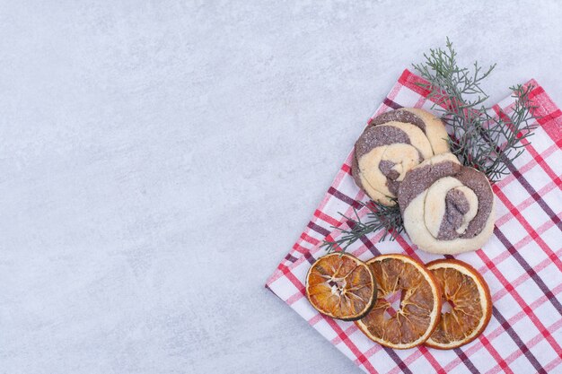 Galletas con naranja seca sobre mantel y rama de pino.