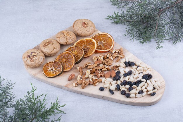 Galletas, naranjas y nueces diversas sobre tabla de madera.