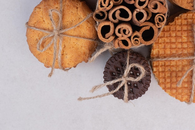 Galletas de Navidad con canela en cuerda sobre mesa blanca.