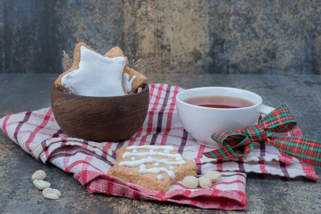 Galletas de Navidad en un tazón de madera con una taza de té sobre un mantel.