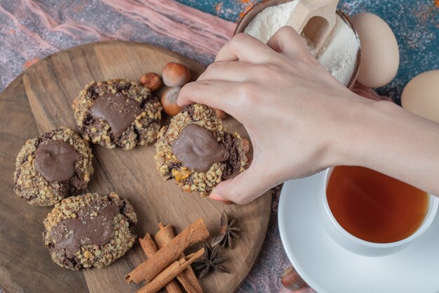 Galletas de nueces de chocolate sobre una tabla de madera servidas con canela y una taza de té.