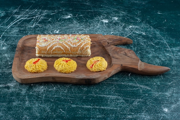 Galletas y pastel de rollo sobre una tabla, sobre la mesa azul.