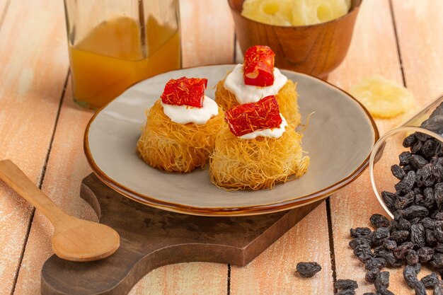 Galletas de pastelería oriental dentro de la placa con crema blanca piña seca y frutos secos sobre la mesa de madera