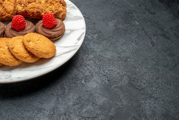 Galletas y pasteles de vista frontal dentro de la placa sobre un escritorio gris