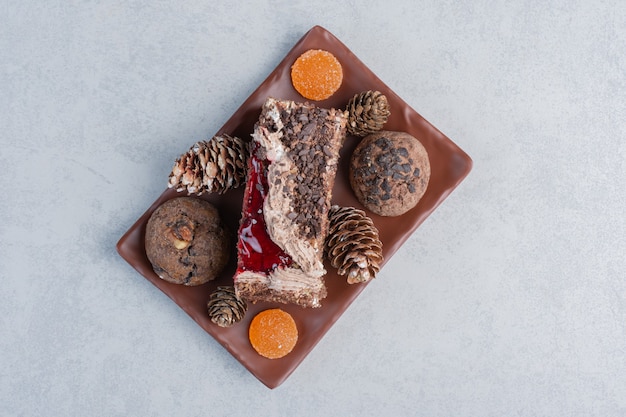 Galletas, piñas, caramelos de gelatina y un trozo de pastel en un plato sobre la superficie de mármol