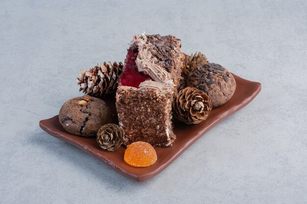 Galletas, piñas, caramelos de gelatina y un trozo de pastel en un plato sobre la superficie de mármol