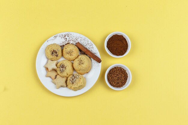 Galletas en un plato con café, canela en rama sobre un fondo amarillo