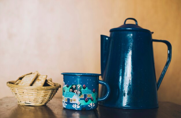 Galletas de queso crujientes finas hechas en casa; Taza y tetera de porcelana en el escritorio contra la pared.