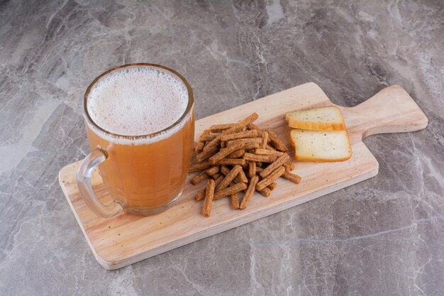 Galletas, queso y vaso de cerveza sobre tabla de madera. Foto de alta calidad