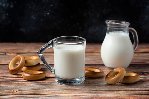 Galletas redondas, taza de vidrio y jarra de leche en la mesa de madera.