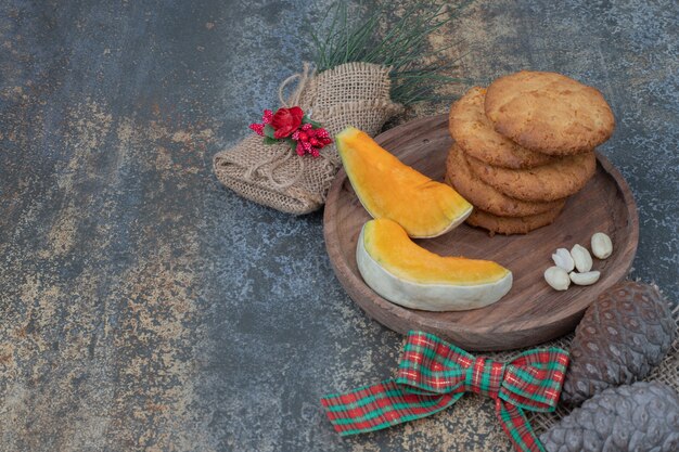 Galletas y rodajas de calabaza en plato de madera decorado con cinta. Foto de alta calidad