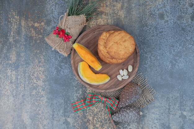 Galletas y rodajas de calabaza en plato de madera decorado con cinta. Foto de alta calidad