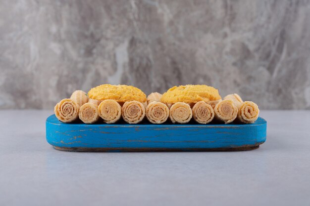 Galletas en rollos de gofres en la bandeja de madera, el mármol.