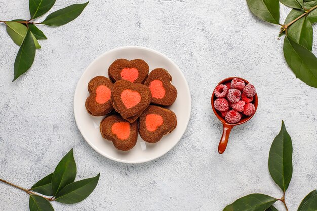 Galletas de San Valentín en forma de corazón con frambuesas congeladas sobre fondo claro