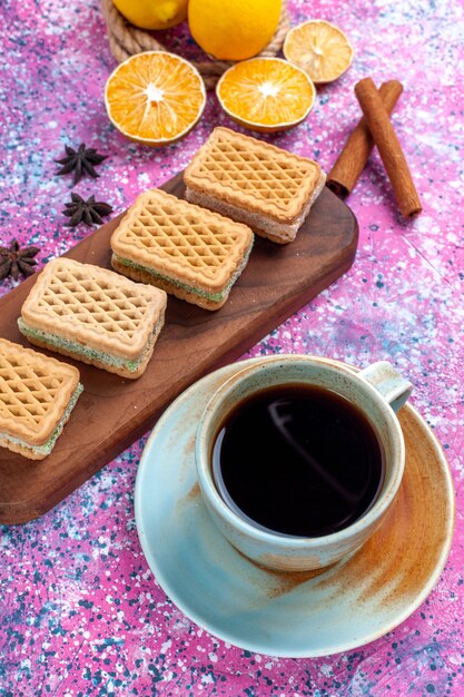 Galletas de sándwich de gofres de media vista superior con relleno de crema de frutas y té en un escritorio rosa claro.